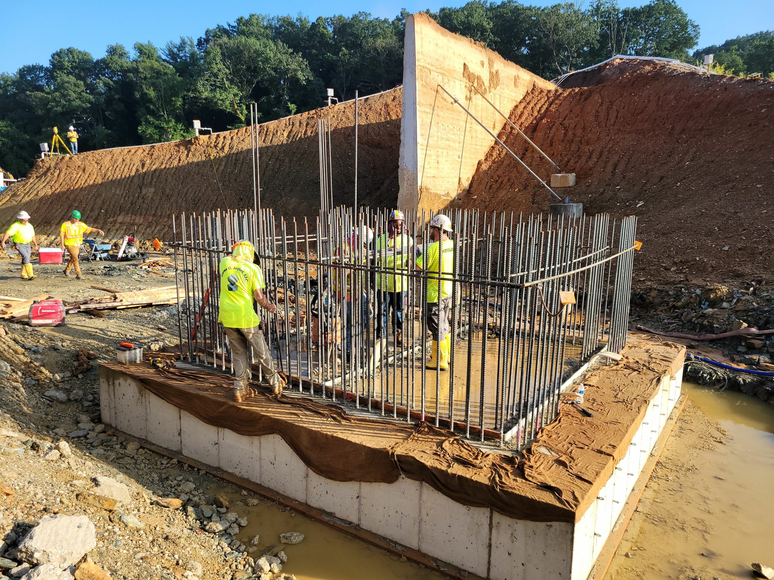 The new dam’s valve tower foundation has been poured and rebar for the valve tower walls are being set. The original 1911 core wall with temporary bracing is in the background.