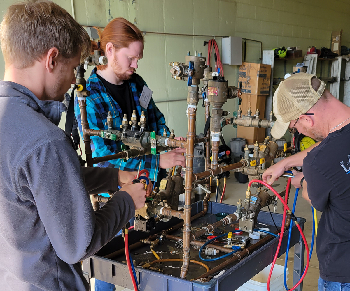 Three people concentrate on their work with pipes and backflow devices.