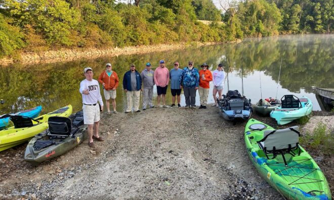 A group of people on the river bank preparing to kayak.