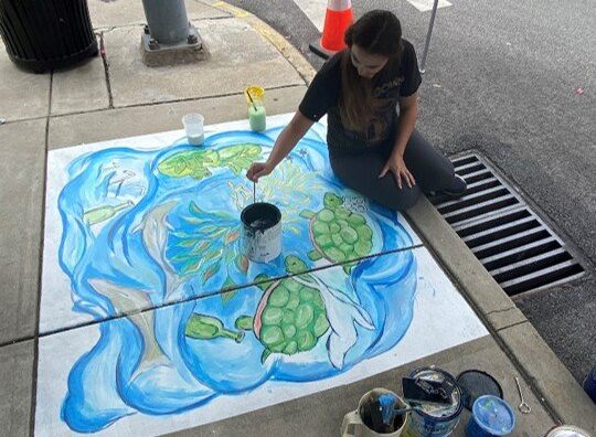 A girl painting a mural on the sidewalk.