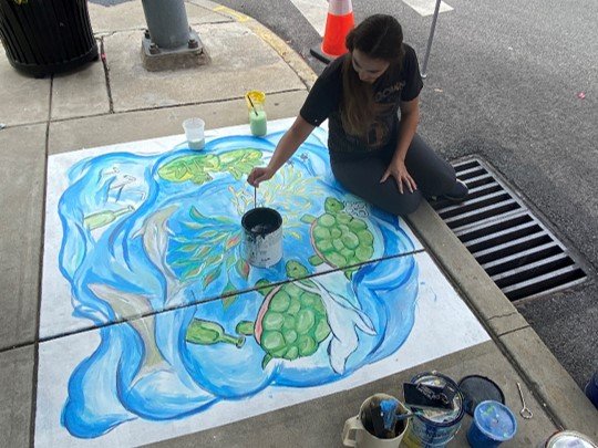 A girl painting a mural on the sidewalk.