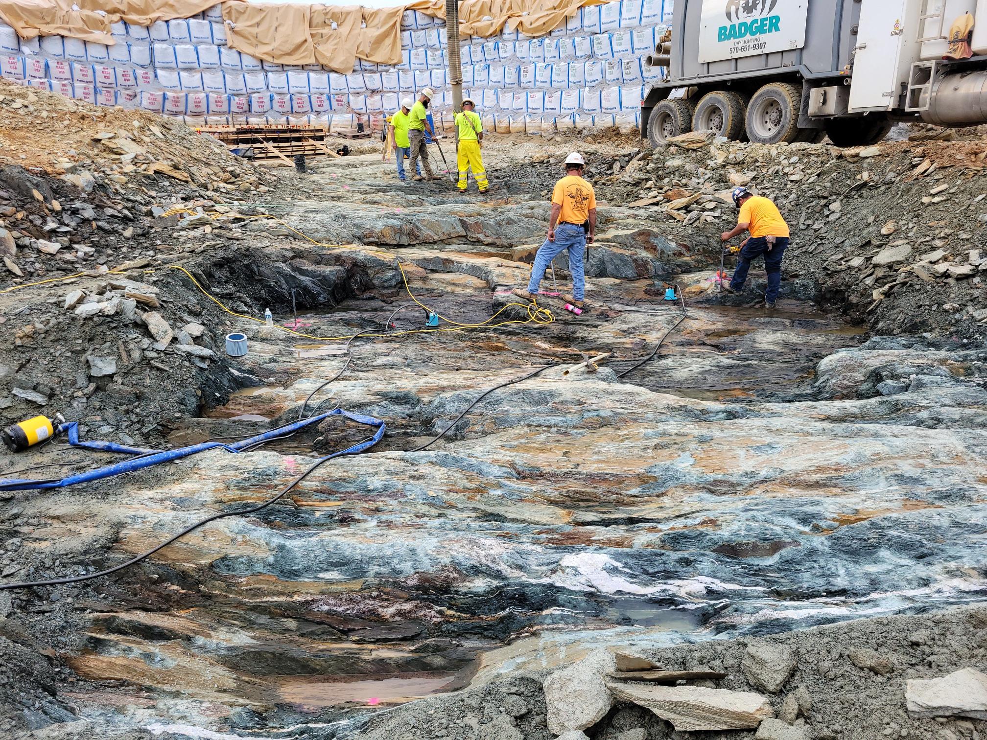 The bedrock at Lake Williams Dam is being prepared for the foundation of a valve tower. The remaining section of Water Street on top of the dam is being dismantled, and preparation to pour the foundation of the 48″ inlet structure is taking place.