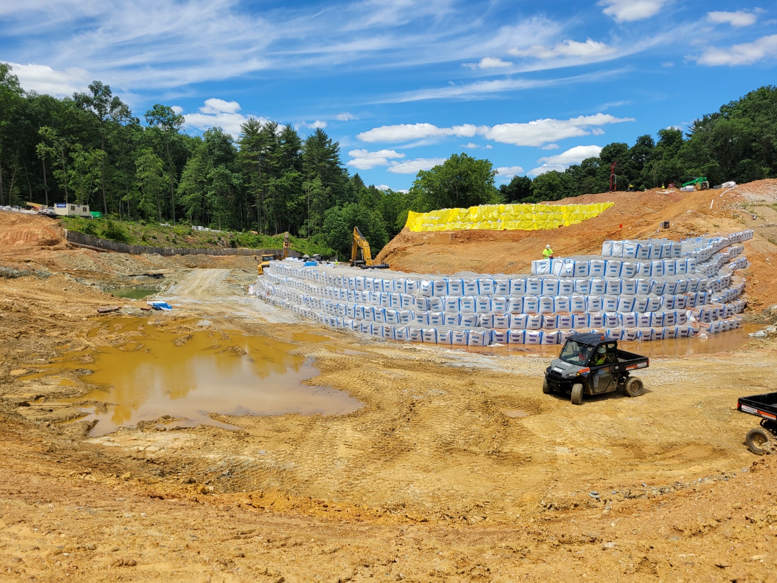 A large, temporary cofferdam to divert excess stream flow is being built around the construction site. A “soil nail wall” to stabilize a sizable excavation on the left side of the dam was just installed, and dewatering wells that will be used to control groundwater levels during construction are being drilled.