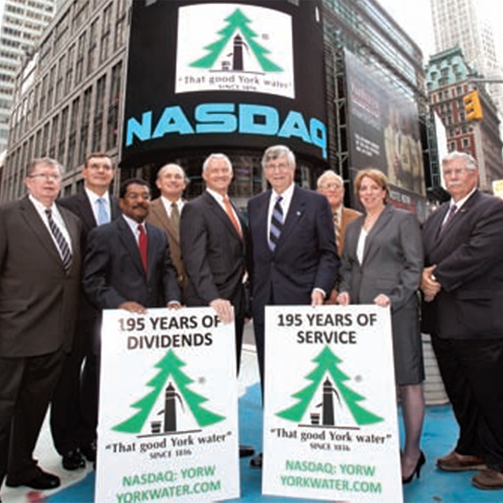 A group of people standing in front of the Nasdaq banner holding signs to celebrate 195 years.