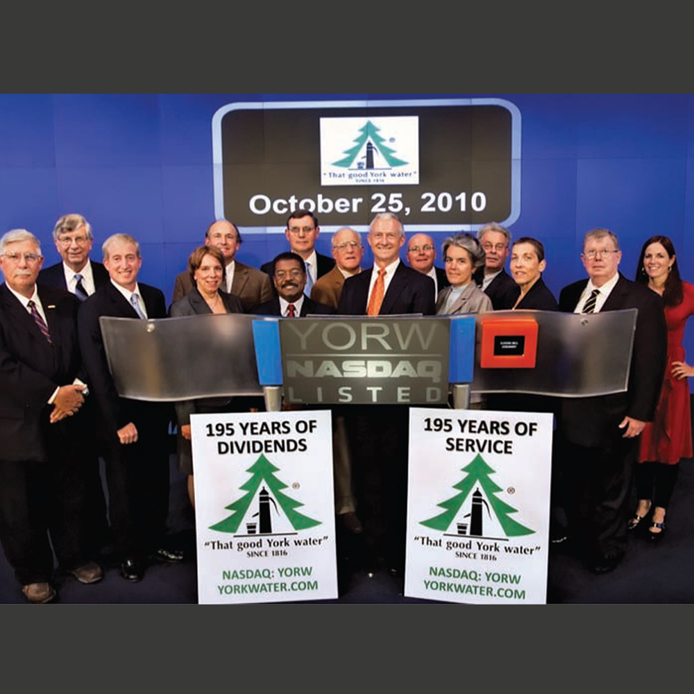 A group of people standing behind a Nasdaq banner holding signs to celebrate 195 years.