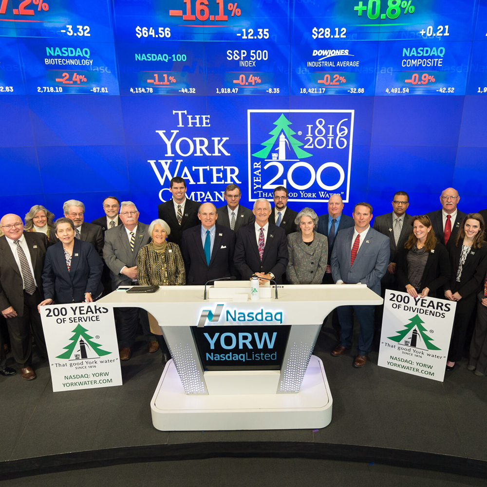 A group of people standing behind a desk with NASDAQ written on the desk and a banner behind them showing 200 years.