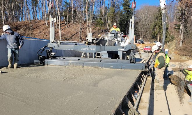 Group of construction workers on a machine putting concrete on the crest of a dam.