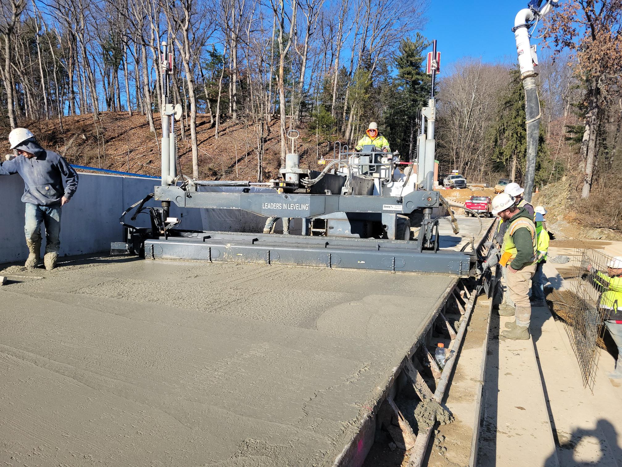 Group of construction workers on a machine putting concrete on the crest of a dam.