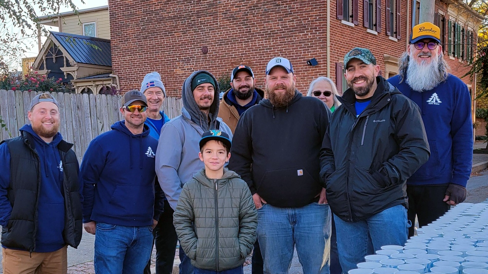 Employees and family members of York Water are pictured at a table filled with little cups of water outside.