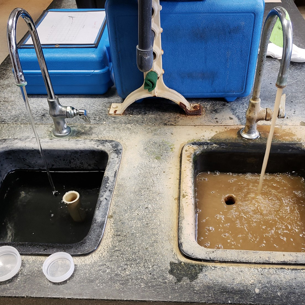 Image of two faucets running water into sinks. One with dirty brown water and the other with clear water.